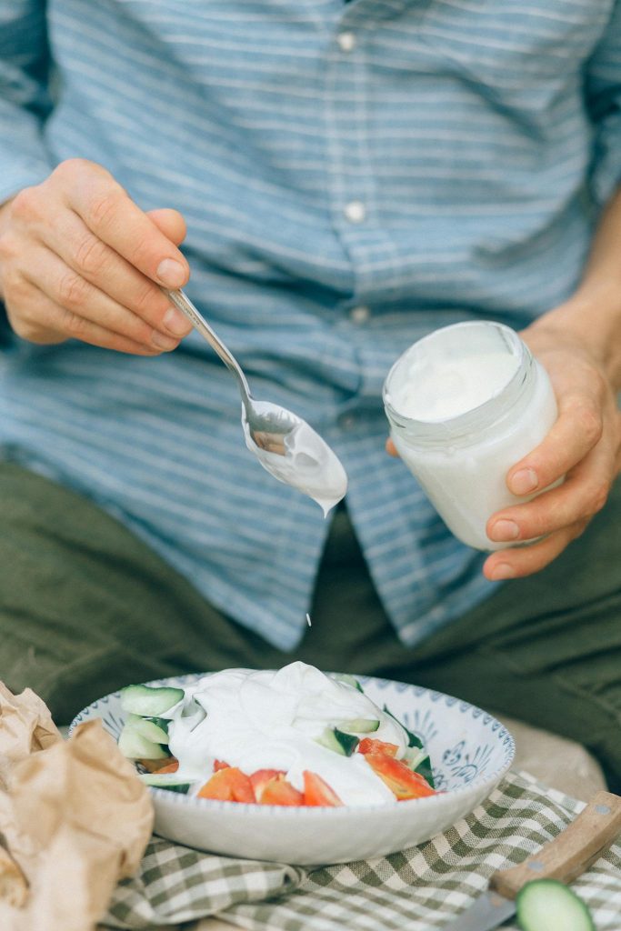 Close-up of a person adding yogurt to a fresh summer salad.