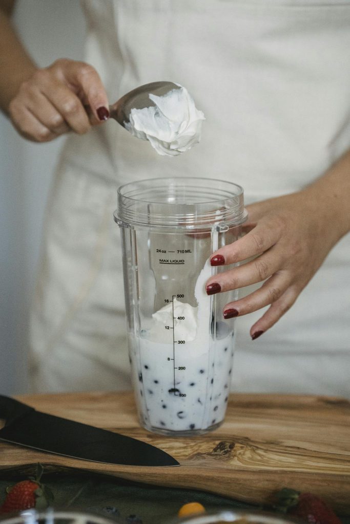 Close-up of hands making a creamy blueberry yogurt smoothie in a glass cup.